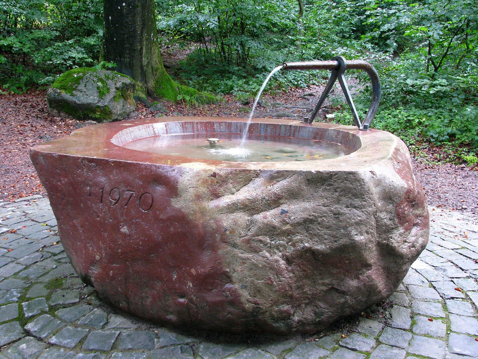 Steinbrunnen mit fliessendem Wasser im Wald am Adlisberg.